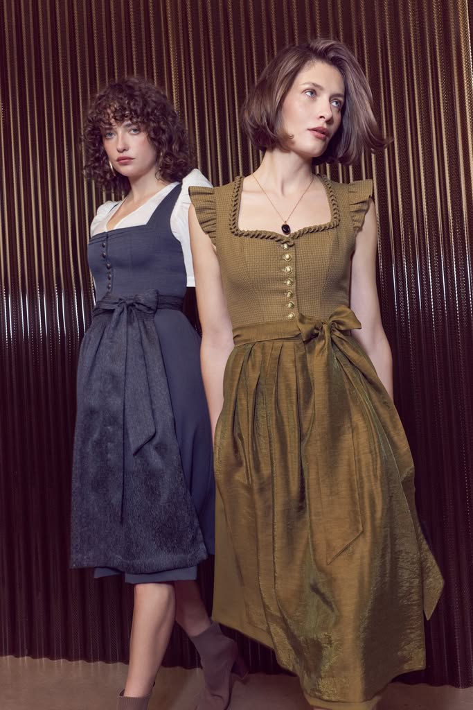 Dirndl in Dunkelblau und Olivgrün, zwei Frauen vor dunkler Wand